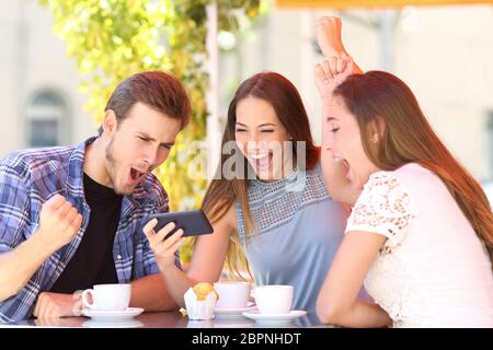 Drei aufgeregt Freunde feiern Gute Nachrichten ansehen smart phone Medien Inhalt in einem Coffee Shop Stockfoto