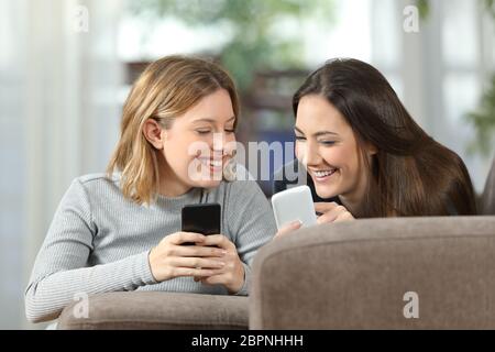 Zwei Mitbewohner sprechen über Inhalte auf ihren Smartphones auf einer Couch im Wohnzimmer zu Hause liegen Stockfoto