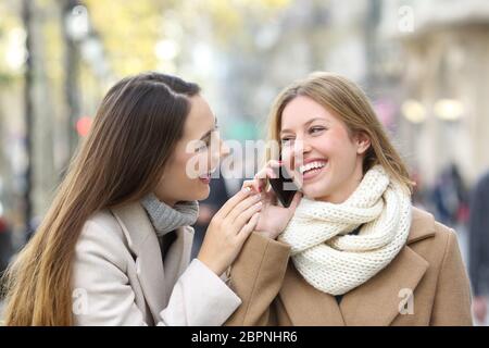 Zwei glückliche Freunde Gespräch am Handy auf der Straße im Winter Stockfoto