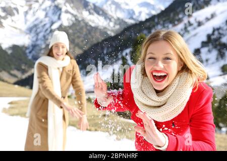 Zwei Freunde scherzen Schneekugeln im Winter in einem verschneiten Berg zu werfen Stockfoto