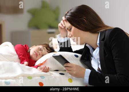 Müde Arbeiter Mutter Anzug nach der Arbeit, während ihre Tochter auf einem Bett in einem Haus-Interieur schläft Stockfoto