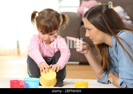 Porträt einer Mutter schelten, ihre kleine Tochter sitzen auf dem Boden im Wohnzimmer zu Hause Stockfoto