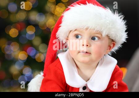 Erstaunt baby Tragen santa claus Kostüm an der Seite Suchen auf einer Couch zu Hause in Weihnachten Stockfoto