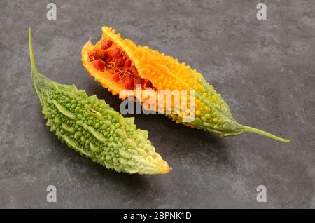 Zwei reife Bittermelonen - gespalten Orange mit roten Samen und warzem grünem Fleisch - auf einem schiefergrauen Hintergrund Stockfoto