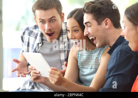 Vier Freunde beobachten Medieninhalte zusammen in einer Tablette sitzen auf einem Sofa im Wohnzimmer zu Hause begeistert Stockfoto