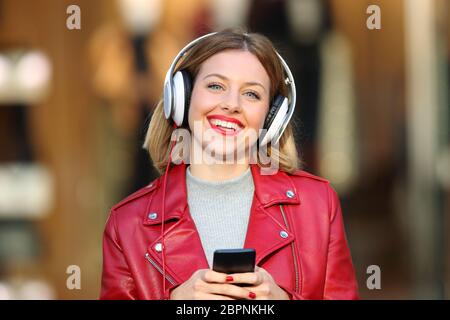 Vorderansicht Portrait Of Happy Mode Mädchen Musikhören von Smart Phone an, die Sie in der Straße Stockfoto