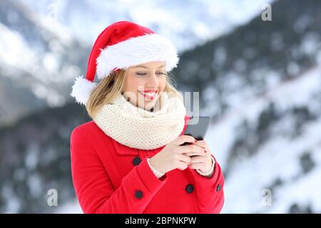 Porträt eines glücklichen Mädchens, das Weihnachtsbotschaften auf einem Smartphone in den Ferien mit einem schneebedeckten Berg im Hintergrund sendet Stockfoto