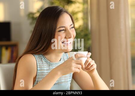 Fröhliches attraktiv und nachdenklich Mädchen hält eine Tasse Kaffee im freien Blick durch das Fenster mit einem warmen Licht des Sonnenuntergangs zu Hause Stockfoto