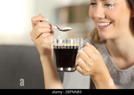 In der Nähe von eine glückliche Frau hand Zucker in Kaffee mit einem Löffel auf einer Couch im Wohnzimmer zu Hause sitzen Werfen Stockfoto