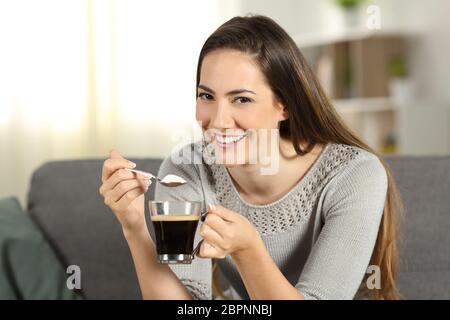 Glückliche Frau Zucker in den Kaffee zu Ihnen schauen auf einer Couch im Wohnzimmer zu Hause sitzen Stockfoto