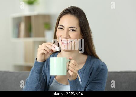 Glückliche Frau Zucker in die Tasse zu werfen, die Sie auf einer Couch im Wohnzimmer zu Hause sitzen Stockfoto