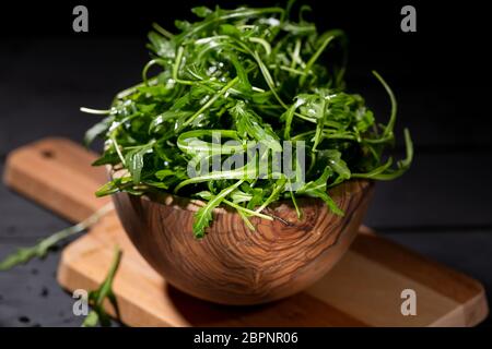Frische Rucola im Holz Schüssel voll mit Rucola Blätter über dem schwarzen Hintergrund, selektiver Fokus Stockfoto