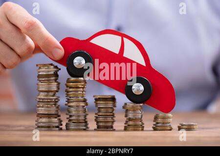Nahaufnahme einer Hand, die einer Person Auto über Rückläufige gestapelte Münzen Stockfoto