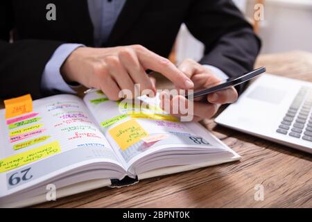 Nahaufnahme eines Kaufmanns Holding Handy Schreiben Zeitplan in das Tagebuch mit Stift Stockfoto