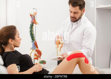 Kinesiologie Taping.Physikalischer Therapeut Anwendung von Kinesiologieband auf den Patienten Knie.Therapeut Behandlung verletzter Knie des jungen Athleten.Post traumatisch Stockfoto