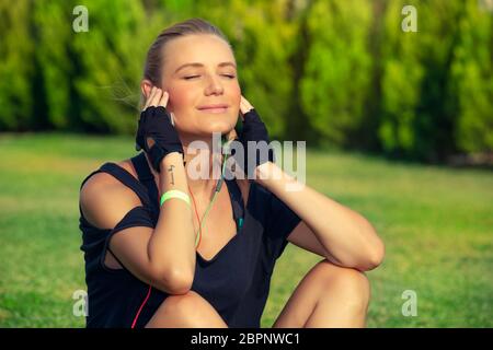 Schöne Mädchen passen sich nach guten Workout, genießen Sonne leuchten mit geschlossenen Augen, bräunen und Musik hören, Meditation im Freien, Harmonie und so Stockfoto