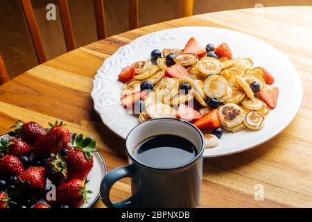 Zum Frühstück gab es winzige Pfannkuchen. Pfannkuchen mit Erdbeeren und Heidelbeeren am Morgen zum Frühstück in der Küche zu Hause gekocht. Hintergrund Der Lebensmittel. Stockfoto