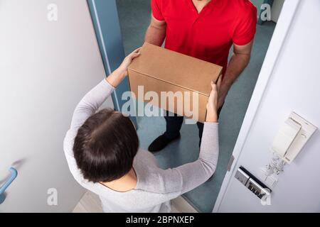 Glückliche junge Frau akzeptieren Karton ab Lieferung Mann Stockfoto