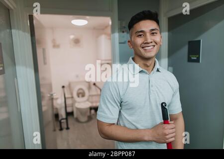 Portrait einer jungen, männlichen Reiniger bei der Arbeit. Er hält einen Mop. Stockfoto