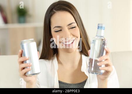 Vorderansicht Porträt einer Frau zwischen Wasser oder Limonade Erfrischung auf einer Couch im Wohnzimmer zu Hause sitzen entscheiden Stockfoto