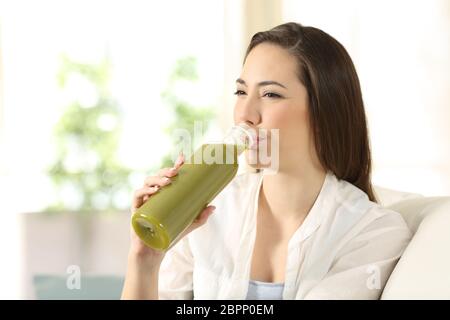 Gerne Frau trinkt ein Gemüse Saft aus der Flasche auf einer Couch im Wohnzimmer zu Hause sitzen Stockfoto