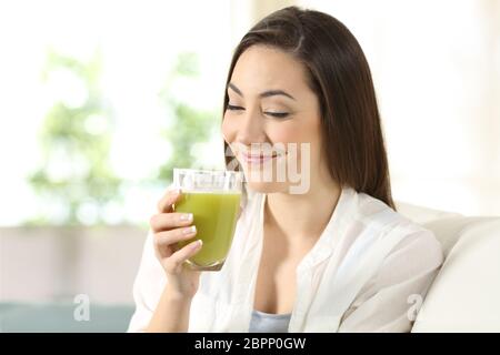 Zufriedene Frau Verkostung ein gutes Gemüse Saft auf einer Couch im Wohnzimmer zu Hause sitzen Stockfoto