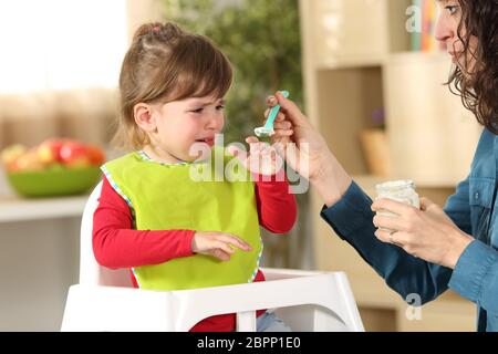 Kleinkind weint Mittags sitzen in einem Hochstuhl im Wohnzimmer zu Hause mit einem heimeligen Hintergrund Stockfoto