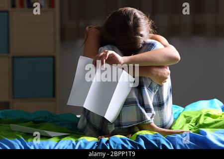 Vorderansicht eines einzigen traurige Teen beklagen nach liest einen Brief mit einem dunklen Licht im Hintergrund auf ihrem Bett sitzen Stockfoto