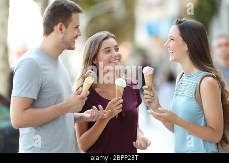 Drei glückliche Freunde sprechen und essen Eis auf der Straße