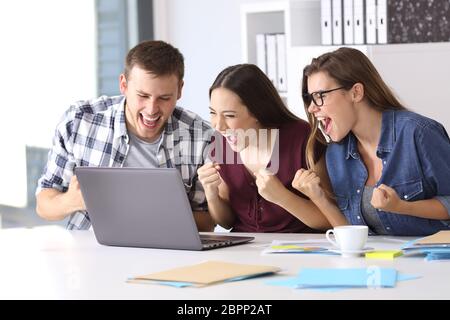 Drei aufgeregt Mitarbeiter lesen gute Nachrichten auf Zeile in ein Notebook in einen Desktop-Computer im Büro sitzen Stockfoto