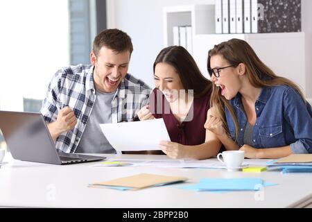 Drei aufgeregt Arbeiter beim Lesen eines guten Ergebnisse Bericht sitzen in einem Desktop im Büro Stockfoto