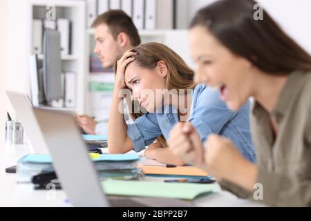 Frustrierte Mitarbeiter neben erfolgreichen einer Lesung Neuigkeiten auf Linie in einem Desktop im Büro sitzen Stockfoto