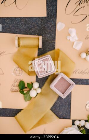 Eheringe in einer Schachtel, Einladungskarten, Seidenband, weiße Rosen auf schwarzem Hintergrund. Ansicht von oben. Stockfoto