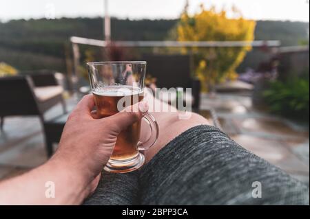 Männchen sitzt im Garten (vereinigtes Königreich) trinken ein frisches Bier genießen Sonnenuntergang mit geringer Tiefe des Feldes verblurten Hintergrund Stockfoto