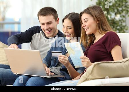 Drei Freunde planen und kaufen eine Reise online mit einer Kreditkarte und einem Laptop sitzt auf einer Couch im Wohnzimmer zu Hause Stockfoto