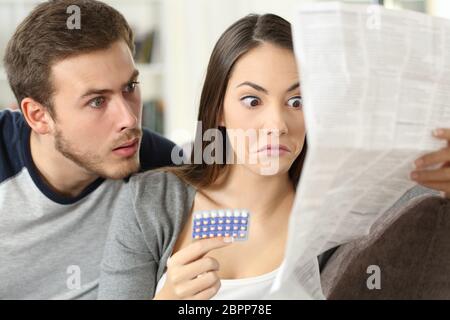 Verdächtiges Paar liest eine Broschüre, nachdem es auf einer Couch im Wohnzimmer zu Hause Verhütungspillen eingenommen hat Stockfoto