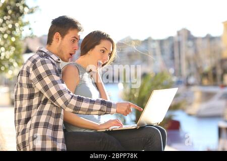 Überrascht Paar im Urlaub gerade online Inhalte in einem Laptop an einem sonnigen Tag Stockfoto