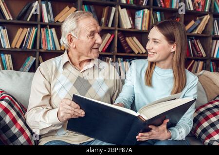 Vater und Tochter zu Hause Bibliothek sitzen halten Fotoalbum diskutieren Erinnerungen Stockfoto