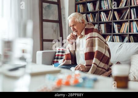 Der ältere Mann allein sitzt in der Bibliothek mit karierten Husten bedeckt Stockfoto