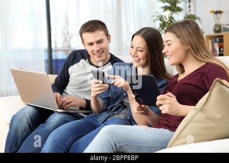 Drei glückliche Freunde teilen Online Inhalte mit mehreren Geräten sitzen auf einem Sofa zu Hause Stockfoto