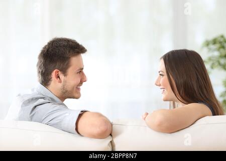 Seitenansicht eines Paares oder einer Ehe, die auf einer Couch sitzen und sich zu Hause mit einem weißen Vorhang im Hintergrund anschauen Stockfoto