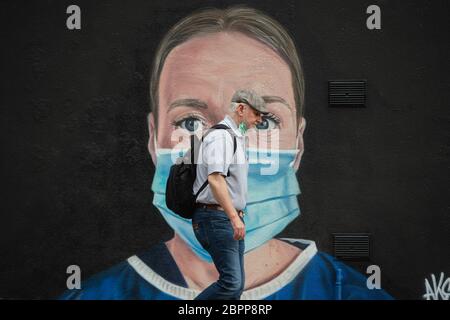 MANCHESTER, Großbritannien EIN Mann in einer falsch verwendeten Gesichtsmaske geht vor einem Wandgemälde einer Krankenschwester mit einer PSA-Gesichtsmaske, das der Künstler Akse im Northern Quarter von Manchester gemalt hat. Dienstag, 19. Mai 2020. (Quelle: Pat Scaasi) Quelle: MI News & Sport /Alamy Live News Stockfoto