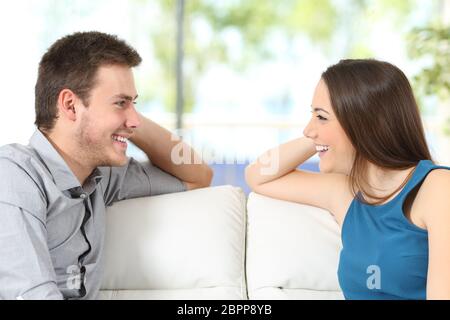 Seitenansicht eines Paares reden und suchen einander zärtlich sitzen auf einer Couch zu Hause mit einem Fenster im Hintergrund Stockfoto