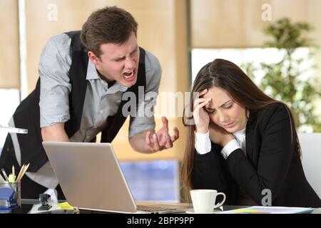 Mobbing mit Out of Control Chef schreien eine gestresste Mitarbeiter in einem Desktop im Büro Interieur Stockfoto