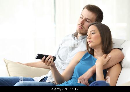 Paar gelangweilt vor dem Fernseher mit einer Hand, die die Fernbedienung sitzt auf dem Sofa zu Hause Stockfoto