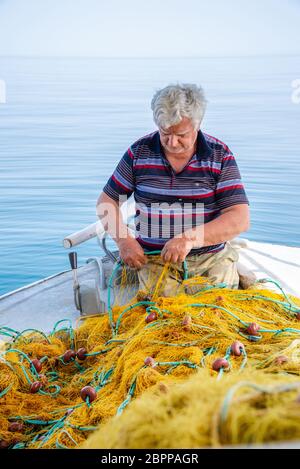 Fischer fischt frische Fische mit gelben Fischernetzen, auf Fischerboot, Kreta, Griechenland. Stockfoto