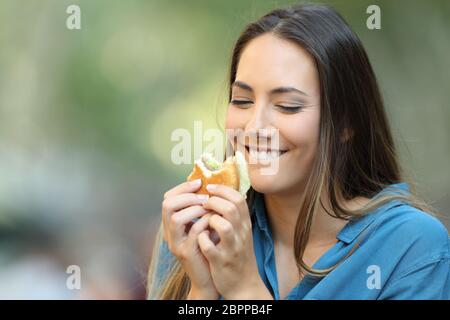 Glückliche Frau essen und suchen einen leckeren Burger auf der Straße Stockfoto