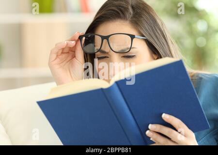 Frau mit Augen, die versuchen, ein Buch zu Hause zu lesen Stockfoto