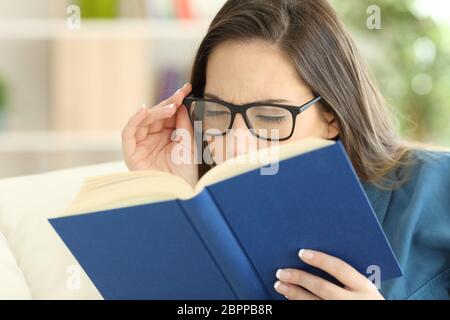 Frau mit einer Überanstrengung der Augen ein Buch lesen Brille zu Hause tragen Stockfoto