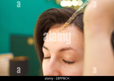 Make-up Künstler Anwendung kosmetisches Öl auf Gesicht der jungen Frau. Aufbringen von Make-up-Flüssigkeit Foundation Stockfoto